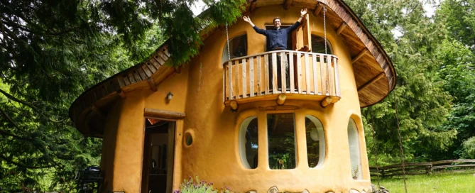 Man With Arms Outstretched Outside of Cob House