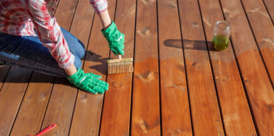 woman treating wood and applying outdoor defense oil into bare wood deck