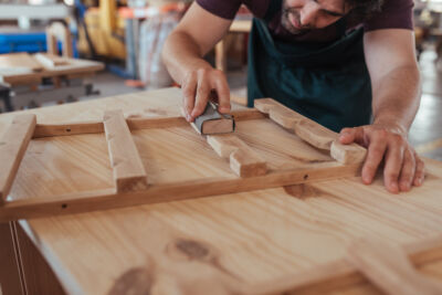 Craftsman skillfully sanding a piece of wood in his workshop, showing how woodworking techniques like this improve the overall finish of the piece.