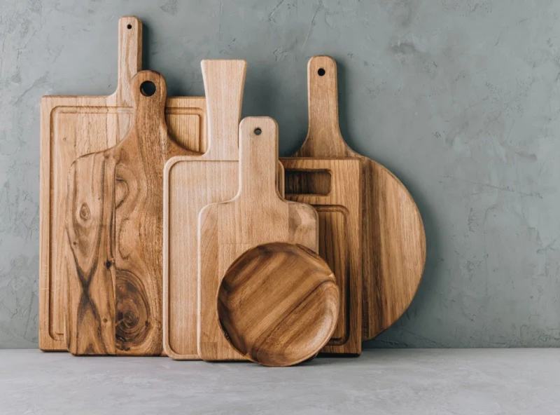 A collection of assorted wooden cutting boards and a small wooden plate leaning against a gray textured wall.